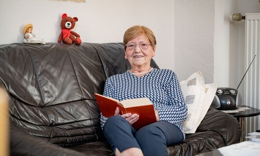 Bewohnerin sitzt lesend auf dem Sofa