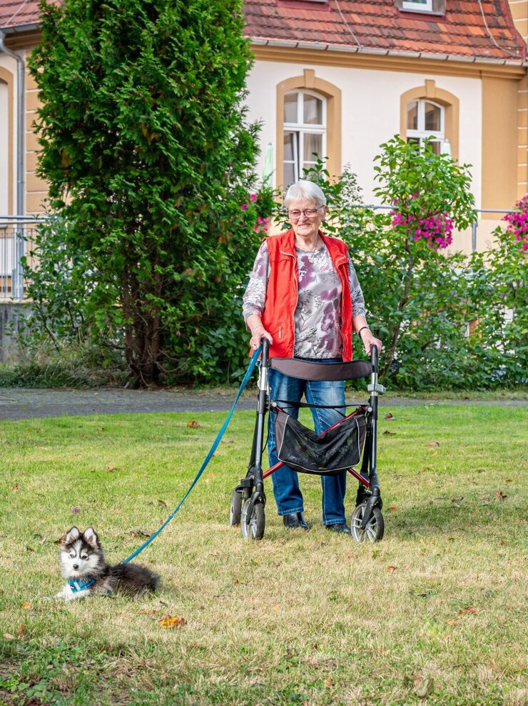 Bewohnerin mit Rollator und Hund im Garten