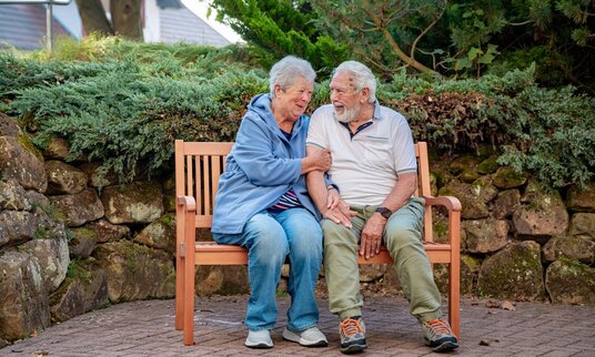 Bewohner-Ehepaar sitzt im Garten auf der Bank